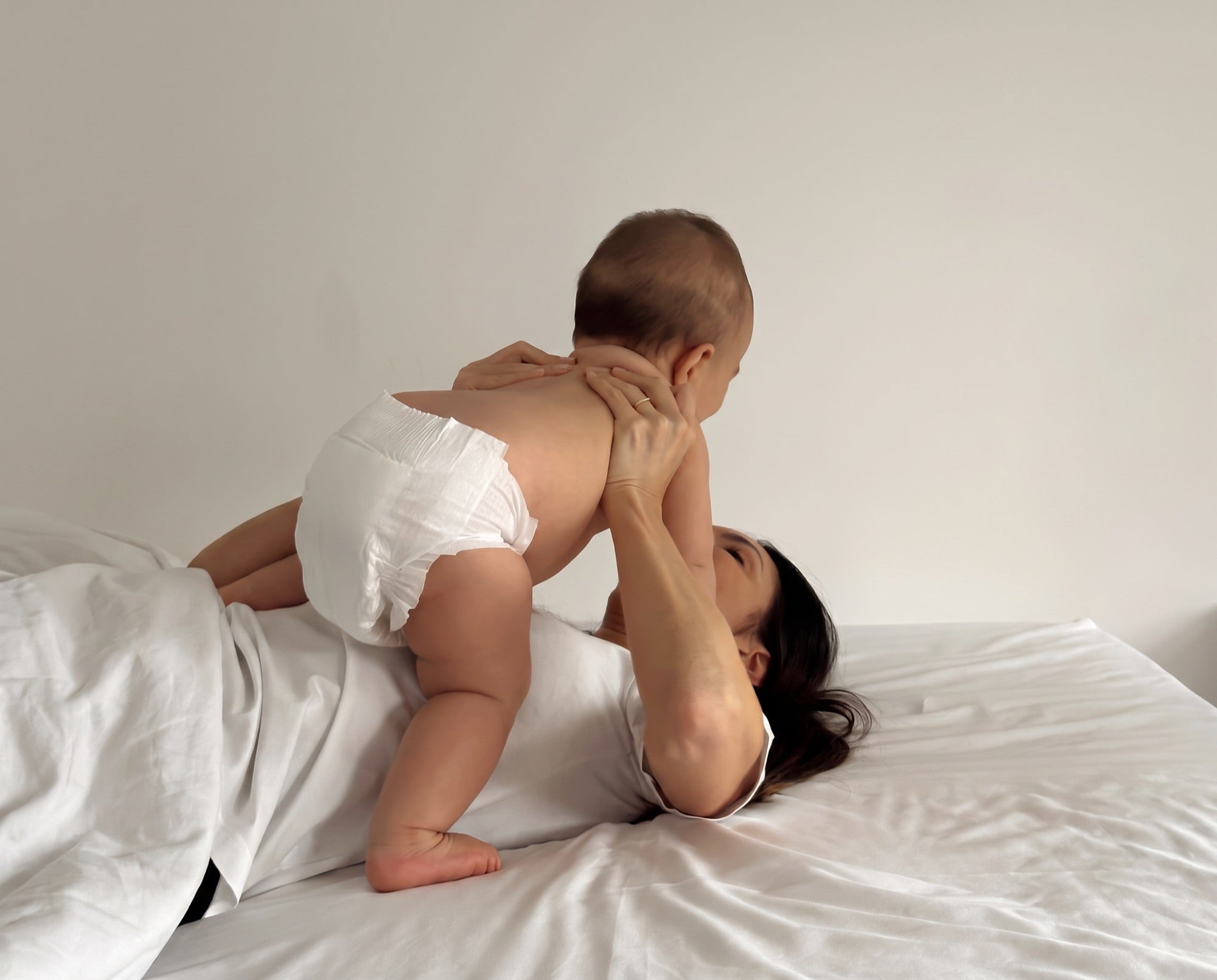 Mãe deitada na cama brincando com o bebê de fralda Pato Jack